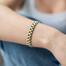 Load image into Gallery viewer, Close-up of a person's wrist wearing a gold and silver bracelet with a blurred background.
