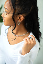 Load image into Gallery viewer, Woman wearing glasses, a silver necklace, and silver earrings with a neutral background
